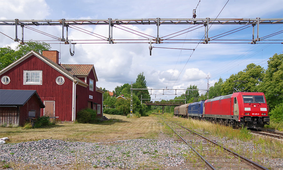 Två ellok typ 185 passerar Vrena med ett två vagnar kort godståg från Borlänge till Oxelösund. Stationshuset från 1875 finns ännu kvar. Foto i juli 2017, Markus Tellerup.
