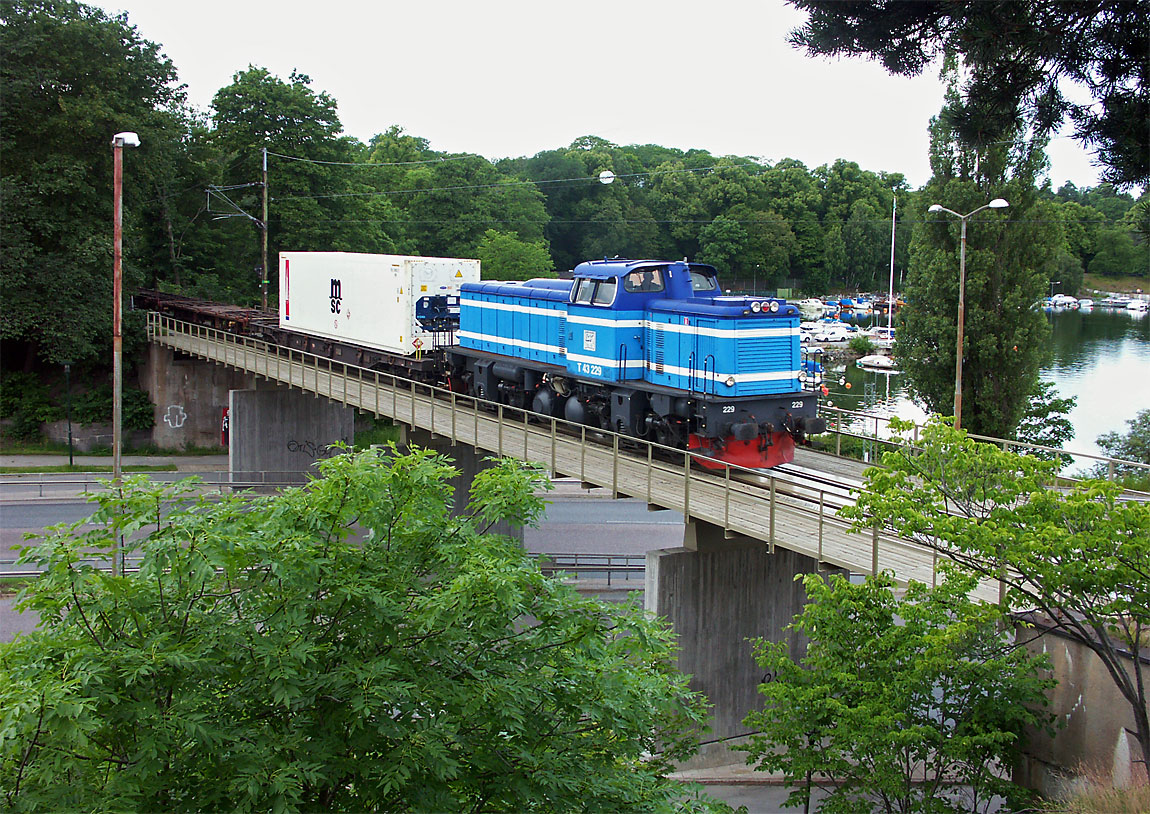Ett tåg draget av ett T43-lok korsar Norrtäljevägen med Brunnsviken i bakgrunden. Vid tidpunkten kördes containertåg mellan Älvsjö och Värtan av företaget Rail Combi som senare togs över av CargoNet. Foto 2004, Markus Tellerup.