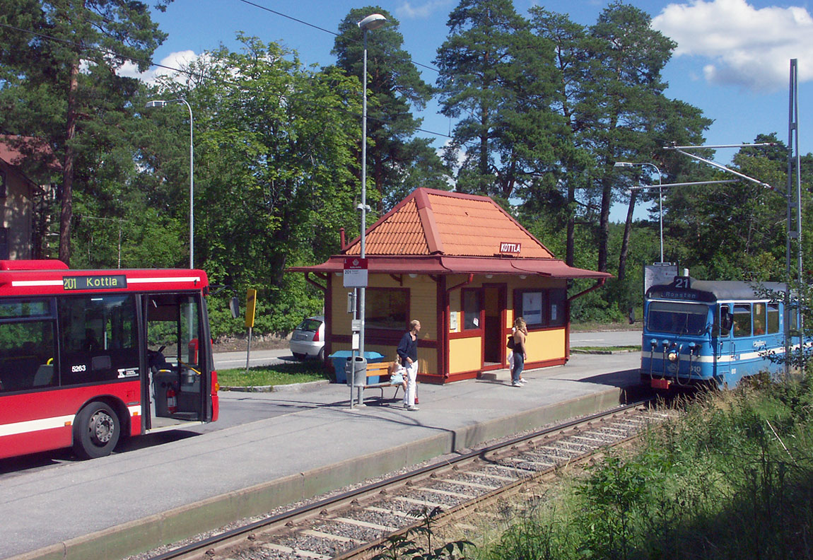 Ett tåg mot Ropsten ankommer Kottla hållplats i juli 2004. Buss 201 till Ropsten via Lidingö Centrum ansluter. Numera finns här två spår men det lilla stationshuset står kvar. Foto Markus Tellerup.