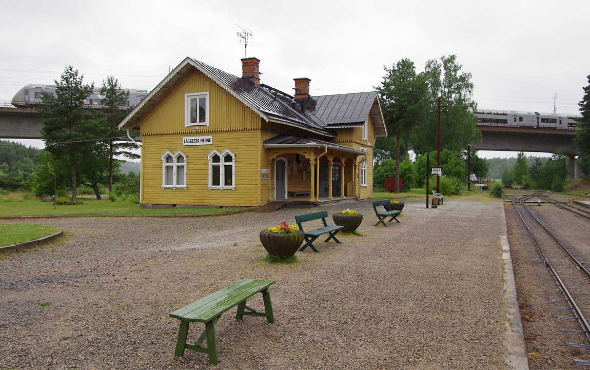 Läggesta Nedre i väntan på att ångtågstrafiken ska starta för dagen en regnig sommardag 2013. På Svealandsbanans viadukt avgår ett X40-tåg mot Stockholm. Foto Markus Tellerup.