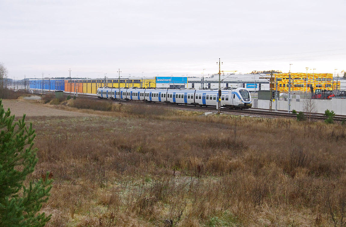 Ett pendeltåg mot Märsta passerar Postnords nya terminal i Rosersberg i november 2014. I full drift ersätter den postterminalerna i både Tomteboda och Uppsala. Foto Markus Tellerup.