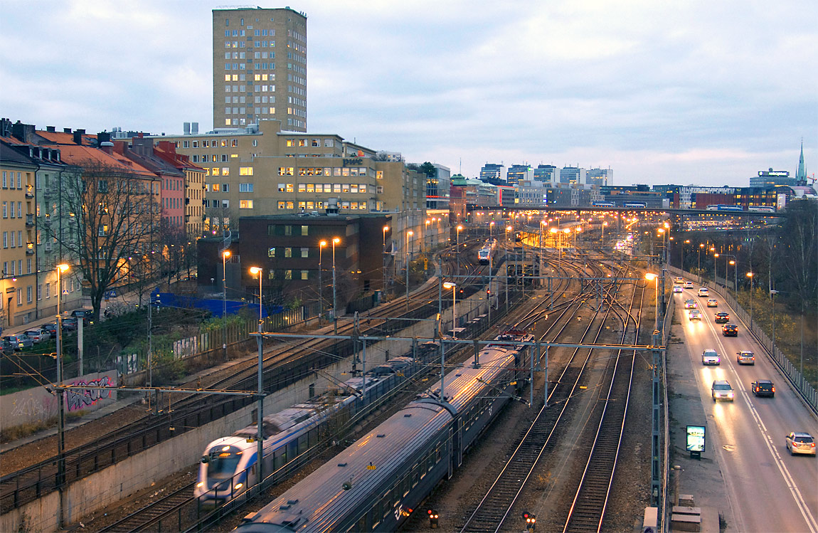 Norr om Stockholm C är pendeltågens spår nedgrävda i ett "tråg" som korsas av de norrgående fjärrtågen och tåg mellan Hagalund och Stockholm C. Bortom serviceplattformarna vid Norra Bantorget syns de fem höghusen vid Hötorget. Foto 2014, Markus Tellerup.