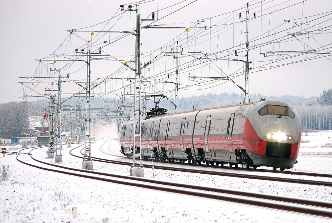 Ett tåg Oslo-Göteborg bestående av en motorvagn typ BM73b passerar Alvhem 2014. Till vänster ansluter banan från Lilla Edet och vid huvudlinjen bakom tåget syns pendeltågshållplatsen Lödöse södra. Foto Markus Tellerup.