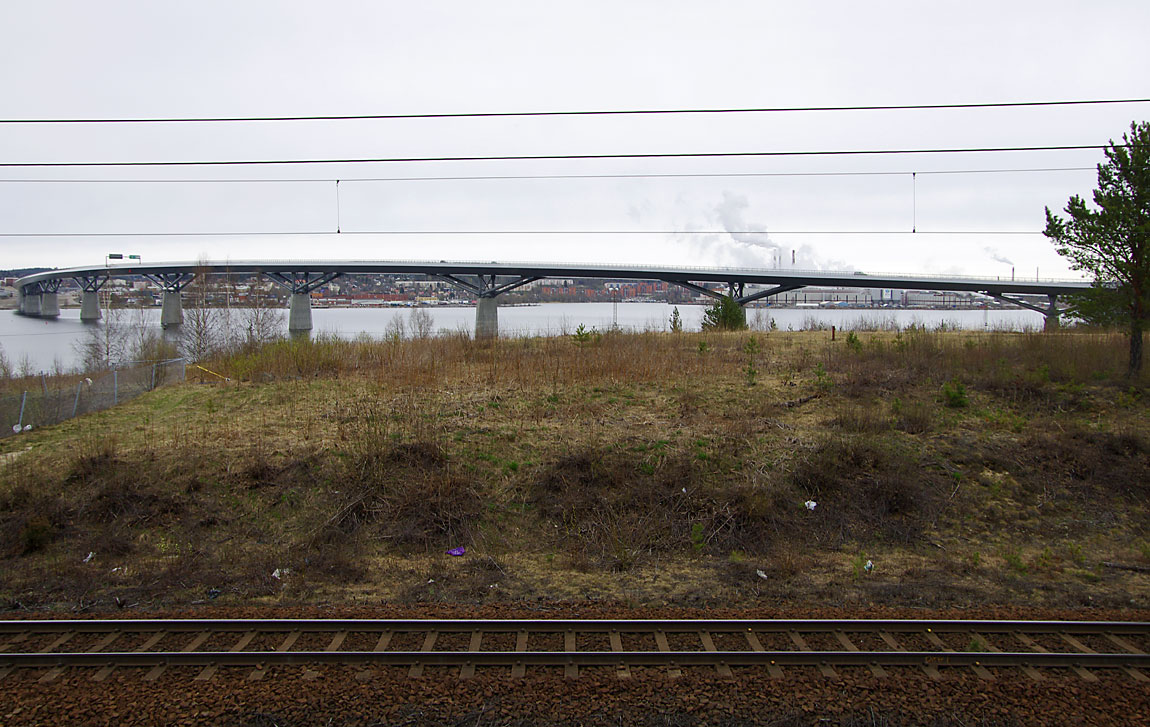 Närmast Sundsvall går Ostkustbanan längs vattnet med utsikt över bland annat den nya Sundsvallsbron och bakom den Ortvikens pappersbruk. Foto 2015, Markus Tellerup.