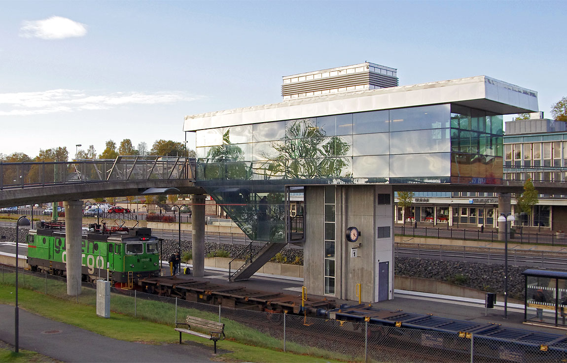 Ett godståg mot Falköping passerar Mullsjö 2015. Här som vid de flesta stationer längs Jönköpingsbanan är det ursprungliga stationshuset rivet. Nybygget med väntsal ovanför perrongen (i viss mån i samma stil som kommunhuset i bakgrunden) invigdes 2005. Foto Markus Tellerup.