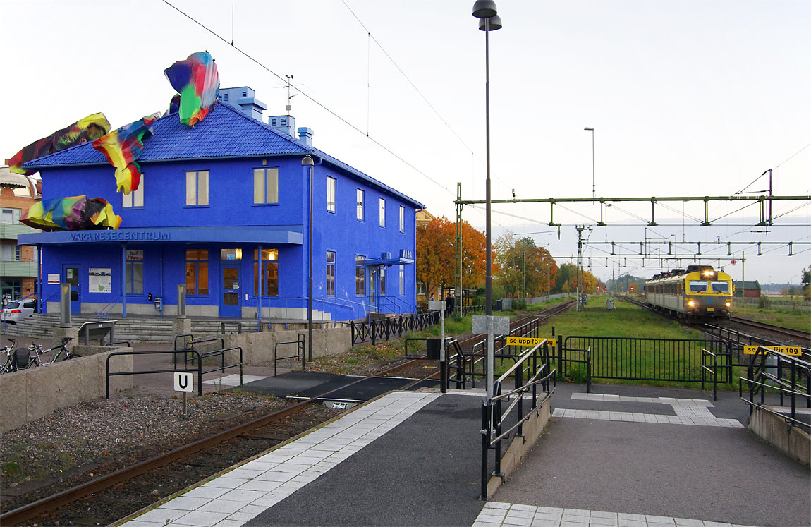 Ett tåg mot Uddevalla bestående av X11 3213 bromsar in vid "Blue Orange", stationshuset i Vara som numera är ett konstverk. Jämför med äldre bild nedan. Foto Markus Tellerup.