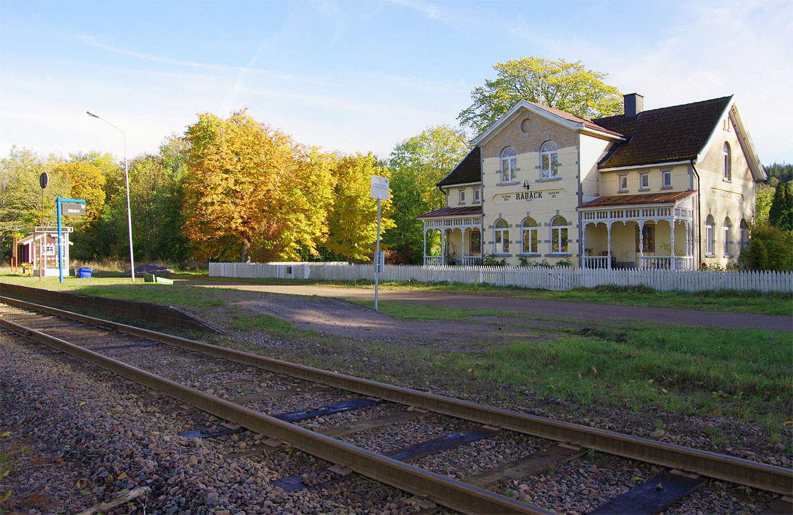 Stationshuset (numera privatbostad) från 1897 och den nuvarande hållplatsen i Råbäck. Huset var ännu ståtligare från början med bland annat tornförsedda paviljonger vid sidan av verandorna. Foto 2015, Markus Tellerup.