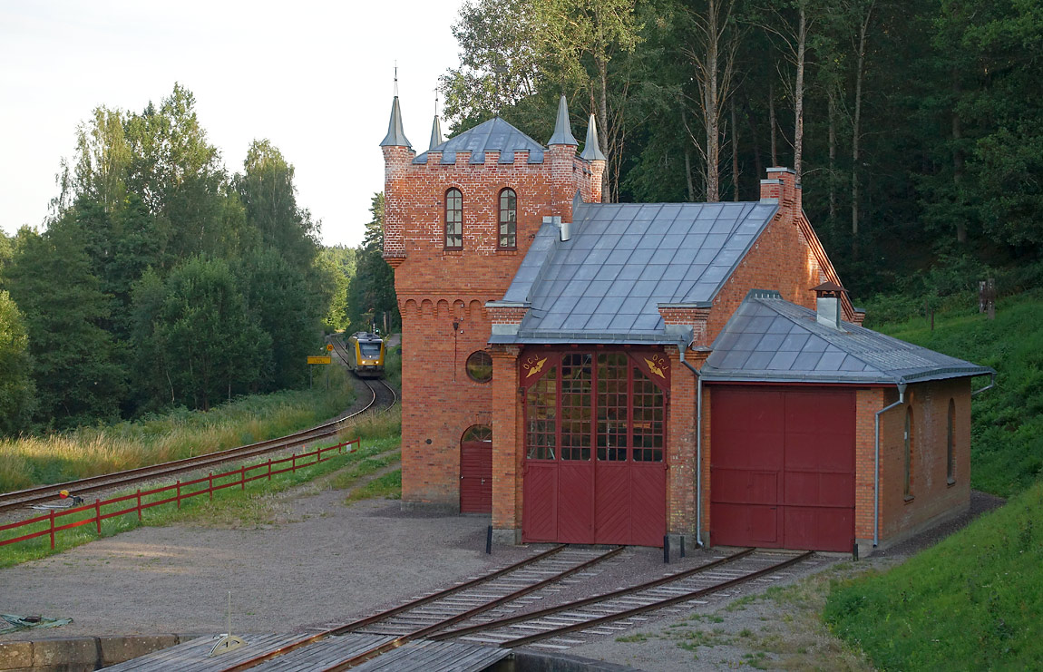 Bild: Det restaurerade lokstallet och vattentornet i Kisa en sommarkväll 2016. Dagens sista tåg Kalmar-Linköping närmar sig söderifrån. Foto Markus Tellerup.