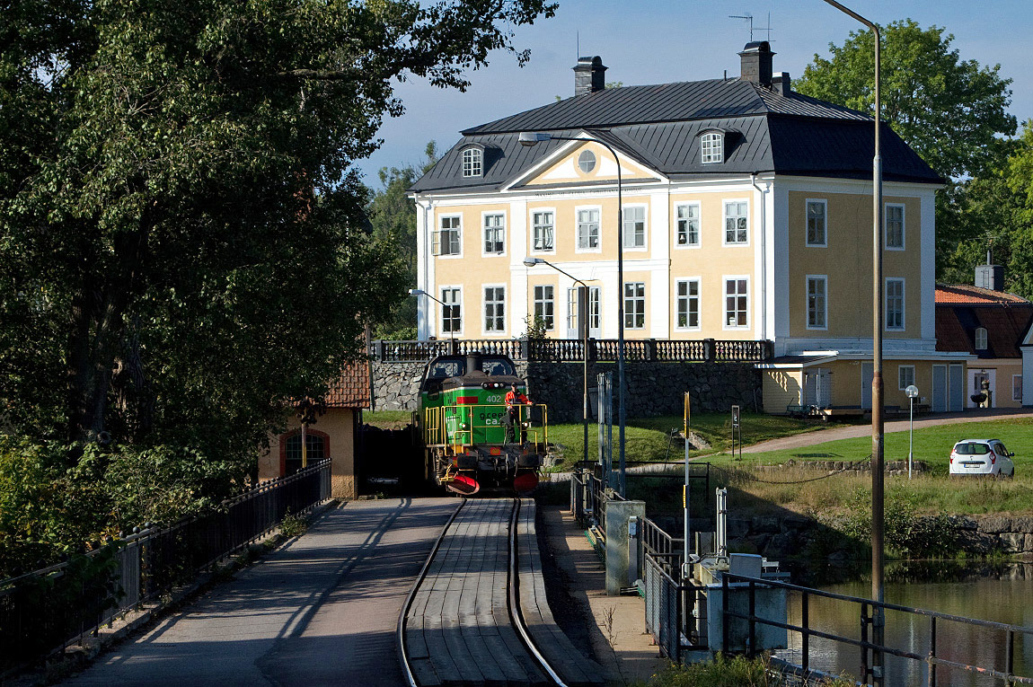 Sidospåret till Ramnäs bruk trafikeras med diesellok, på bilden Td-loket 402. Spåret passerar den så kallade Schenströmska herrgården som tidigare tillhörde bruket och korsar Kolbäcksån på en kombinerad väg- och järnvägsbro. Foto den 13 september 2014, Martin Oscarsson.