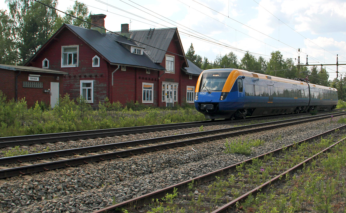 Norrtåg X52 9042 på väg från Umeå till Luleå susar förbi stationshuset i Ekträsk, ett av de kvarvarande stationshusen av Byskemodellen. Foto i juli 2014, Christian Tellerup.
