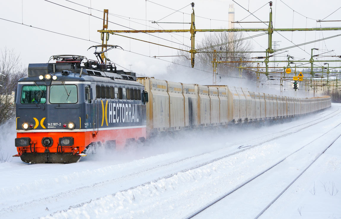 Ett Hector Rail-lok av typ 142 drar ett långt tåg lastat med biobränsle förbi Södertälje syd undre på spåret som leder till Svealandsbanan. Lasten töms i Nykvarn och transporteras sedan med lastbil till Igelstaverket vars skorsten syns i bakgrunden. Foto i februari 2011, Markus Tellerup.