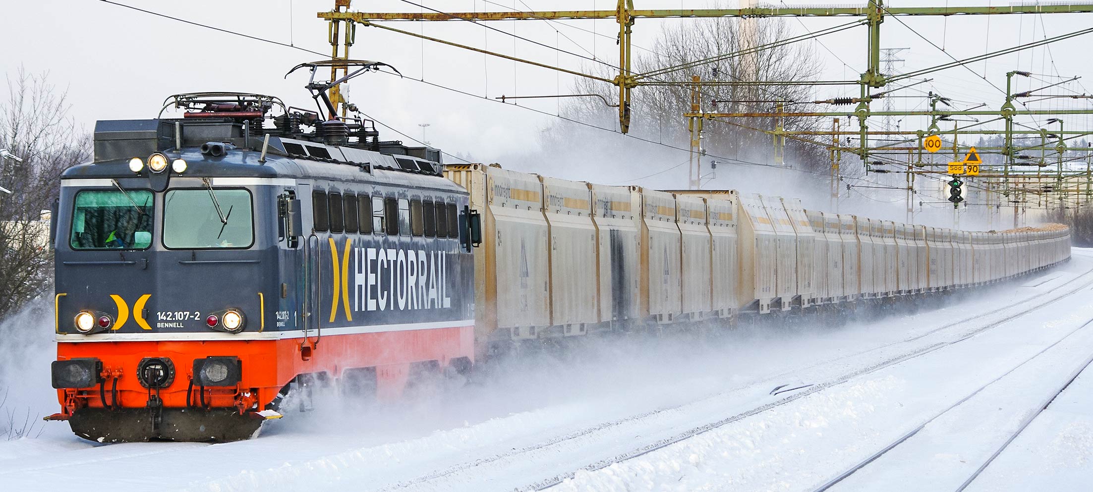 Ett Hector Rail-lok av typ 142 drar ett långt tåg lastat med biobränsle förbi Södertälje syd undre på spåret som leder till Svealandsbanan. Lasten töms i Nykvarn och transporteras sedan med lastbil till Igelstaverket vars skorsten syns i bakgrunden. Foto i februari 2011, Markus Tellerup.